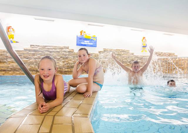 Mädchen sitzen am Poolrand, während Jungs im Wasser planschen