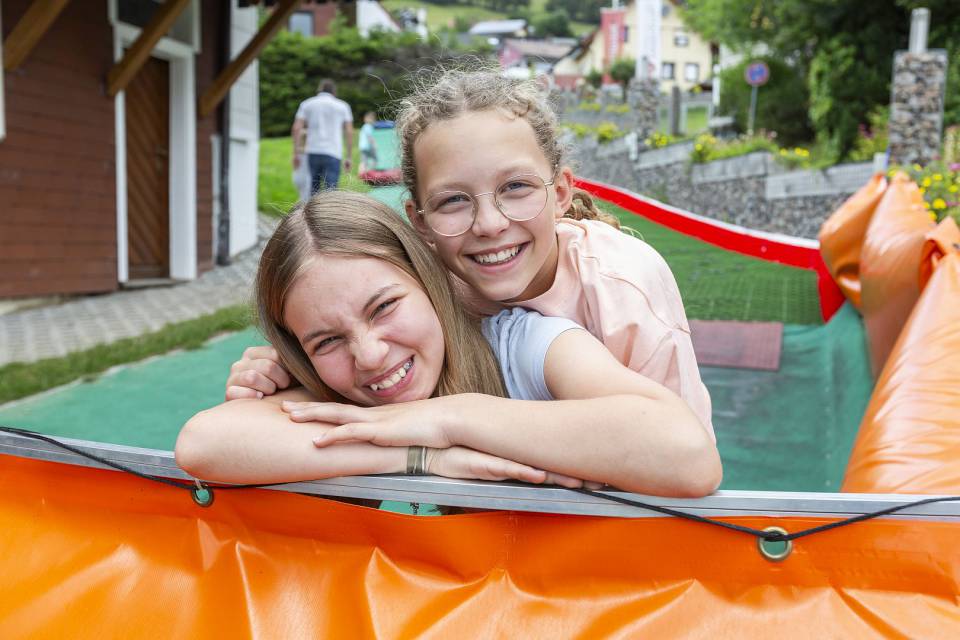 Zwei Mädchen lehnen an einem Gerüst und lächeln in die Kamera