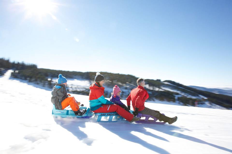 Familie mit zwei Kindern fährt auf drei Schlitten im Schnee den Berg herunter.