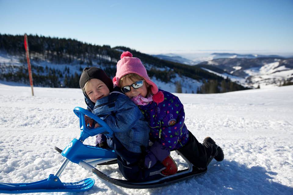 Mädchen und Junge sitzen auf einem Mini-Schneemobil im Schnee