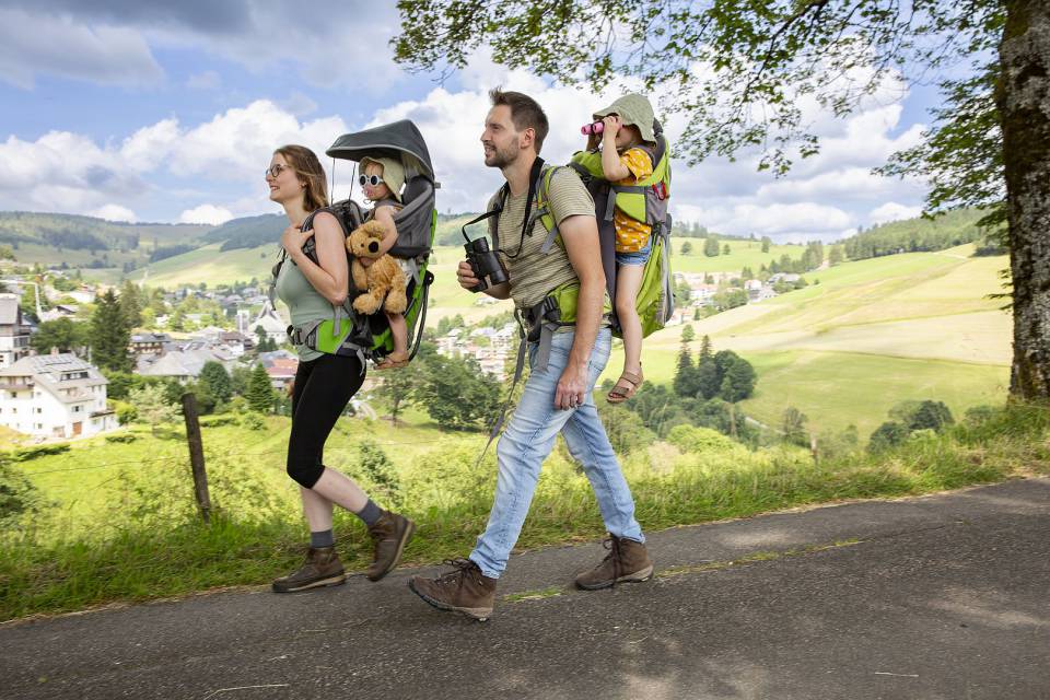 Wandernde Familie mit Kraxe auf einem sonnigen Waldweg