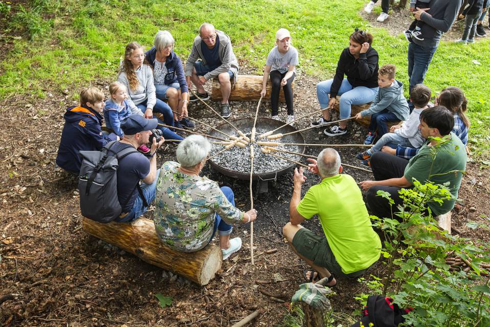 Gruppe von Erwachsenen und Kindern versammelt sich um eine Feuerstelle und grillen Stockbrot.