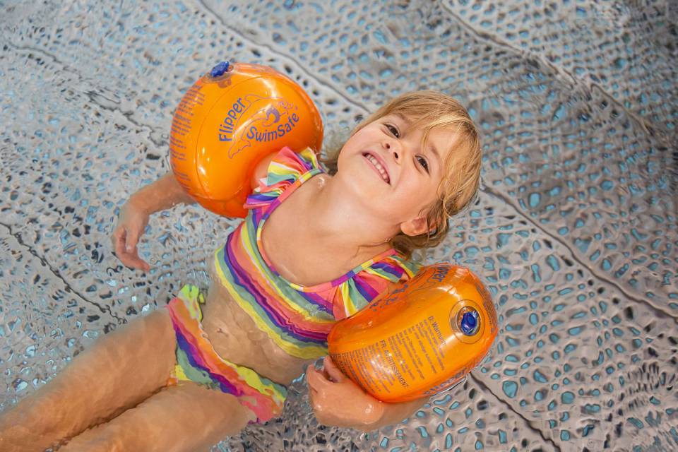 Kleines Kind mit Schwimmflügeln entspannt sich im Wasser.