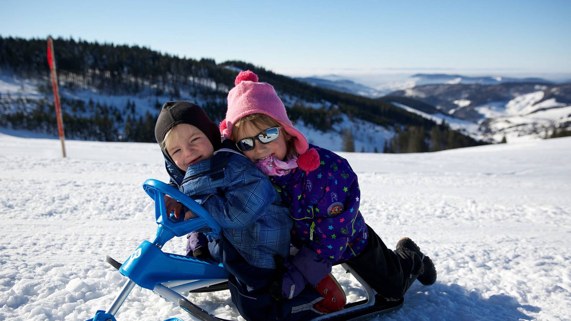 Mädchen und Junge sitzen auf einem Mini-Schneemobil im Schnee