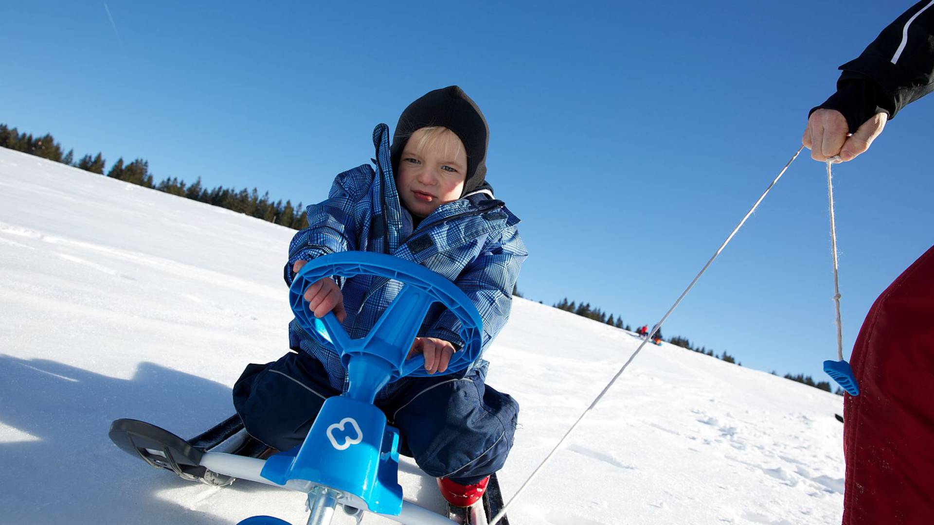 Kleiner Junge wird im Schnee auf einem Schneemobil gezogen
