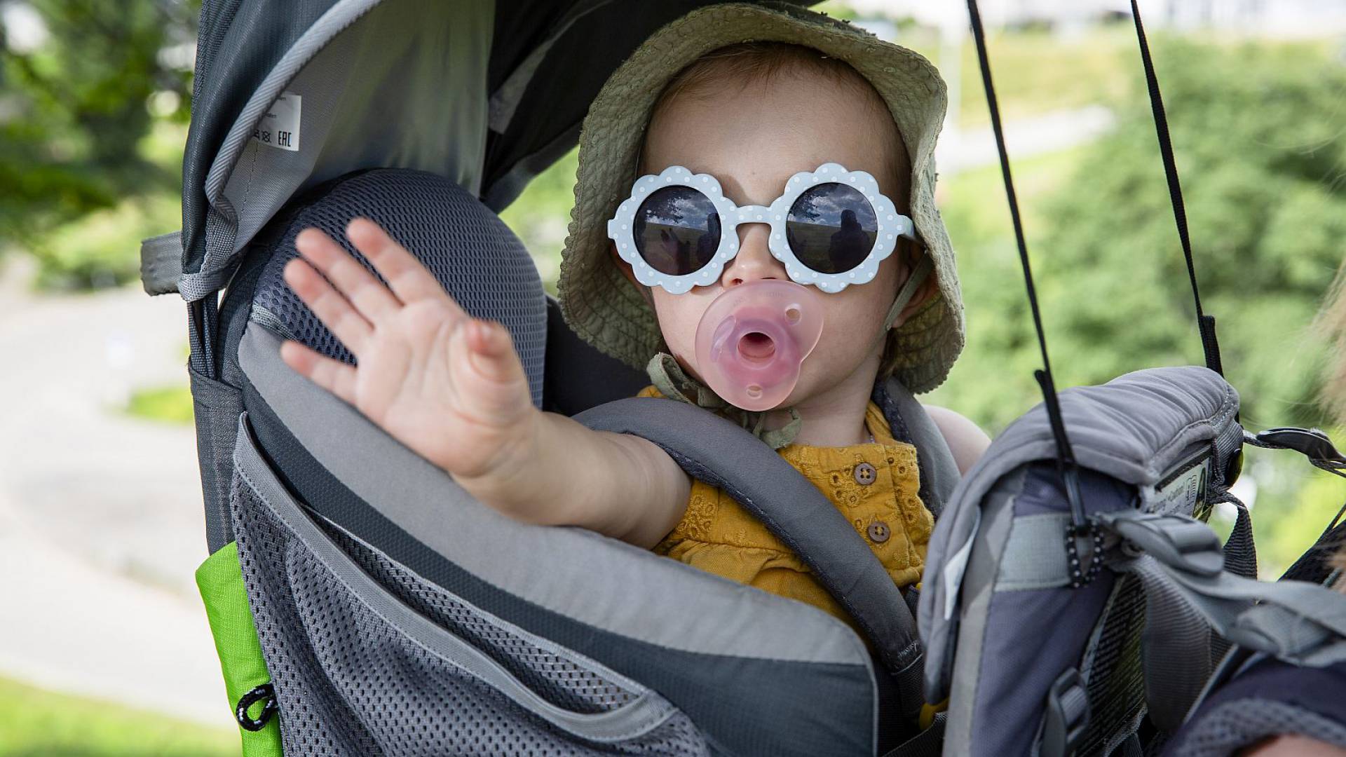 Kleinkind mit Sonnenbrille sitzt entspannt in einer Rückentrage.