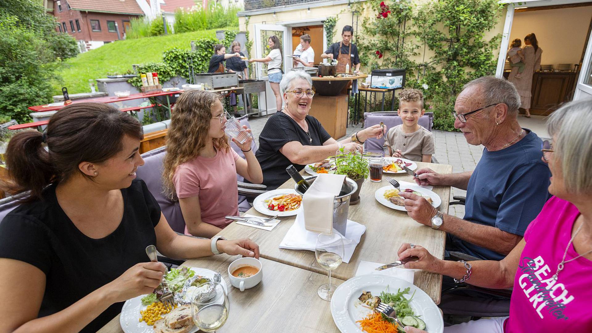Gruppe von Erwachsenen, Kindern und Senioren genießt ein Essen im Garten.