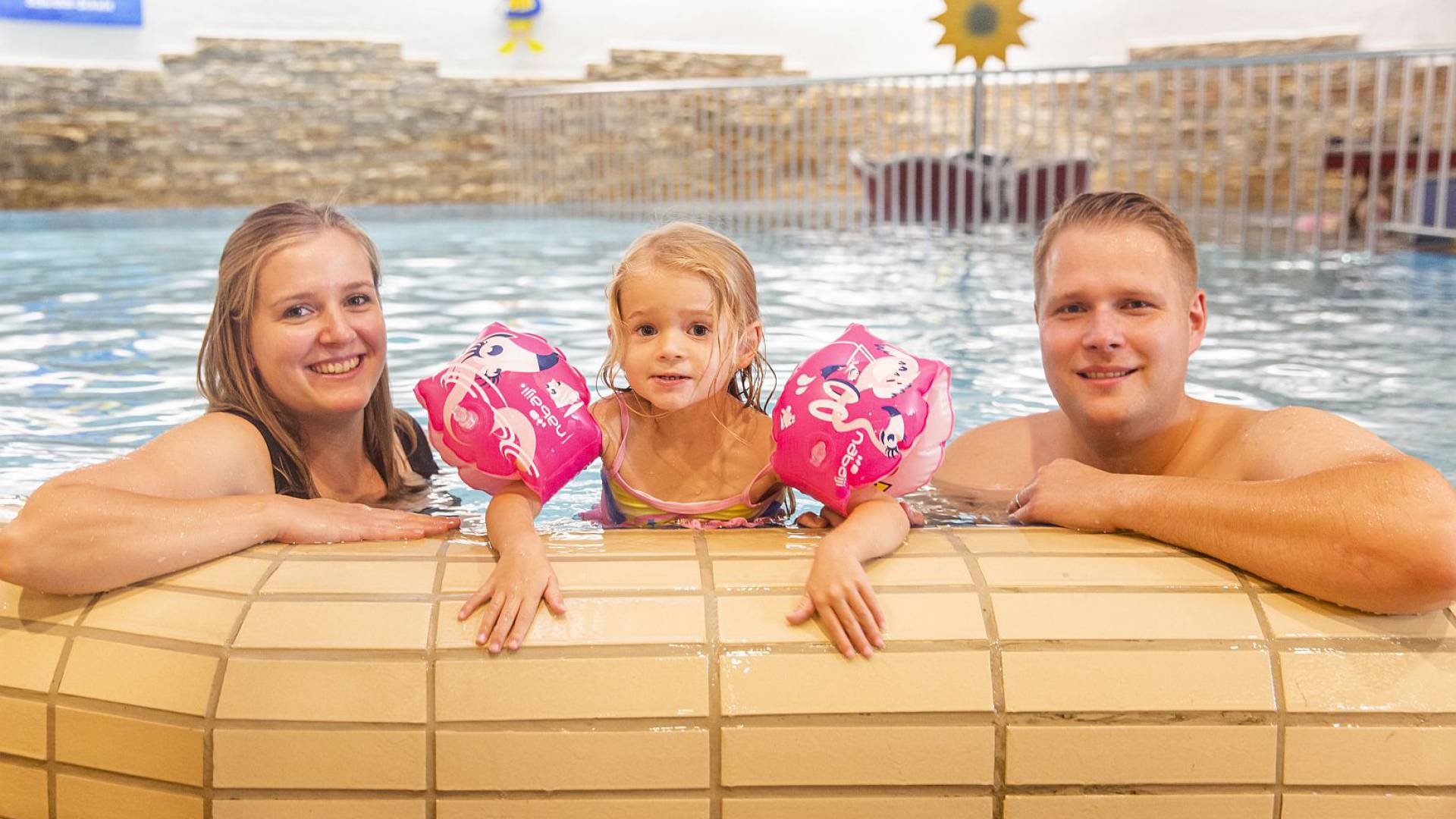 Mutter und Vater stützen sich mit Tochter am Beckenrand an.