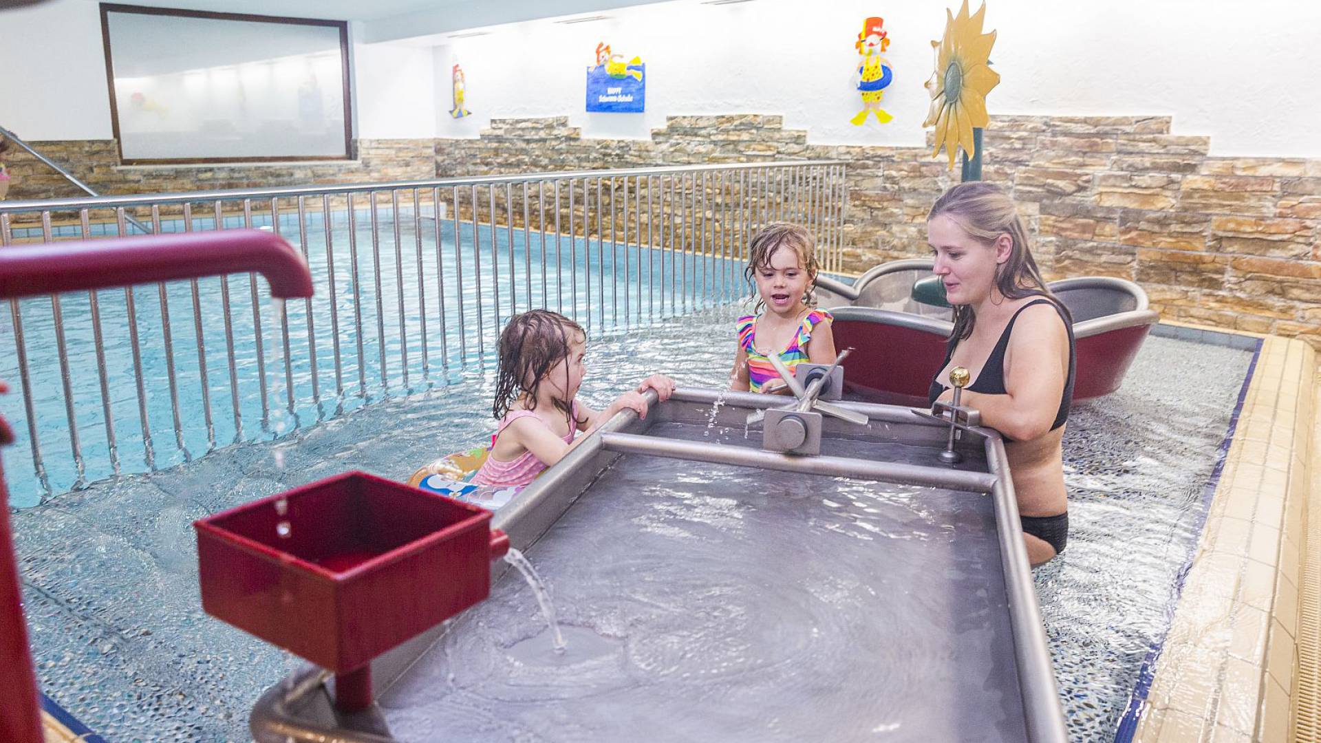 Mutter spielt mit zwei Mädchen am Wasserspielbereich