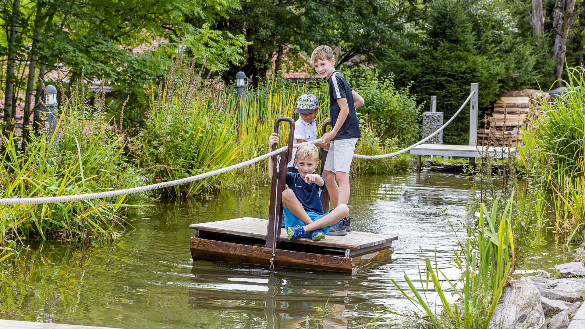 Jungs überqueren einen kleinen Teich mit einer Floßfähre.
