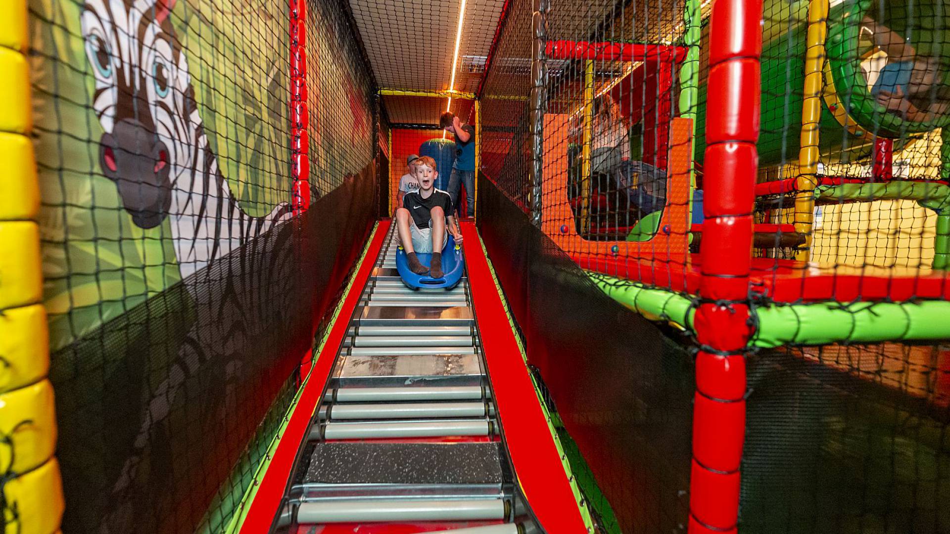 Bunte Indoor-Kletteranlage mit roten Netzen und Röhren.